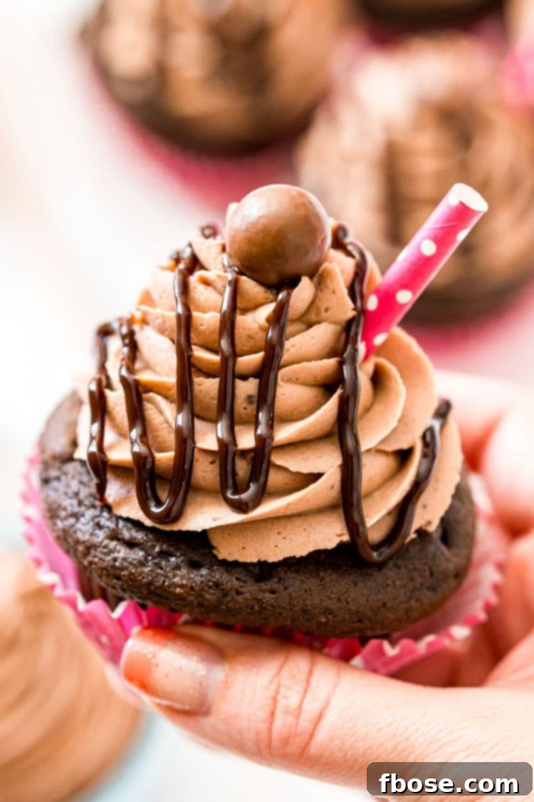 A woman's hand delicately holding a beautifully frosted chocolate cupcake, artfully drizzled with chocolate sauce, ready to be enjoyed.
