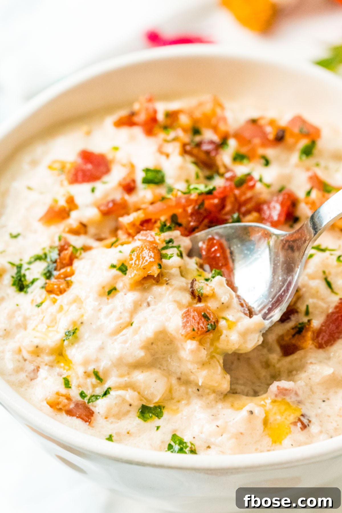 A spoon taking a generous scoop out of a bowl of savory cauliflower chowder, showcasing its rich texture and deliciousness.