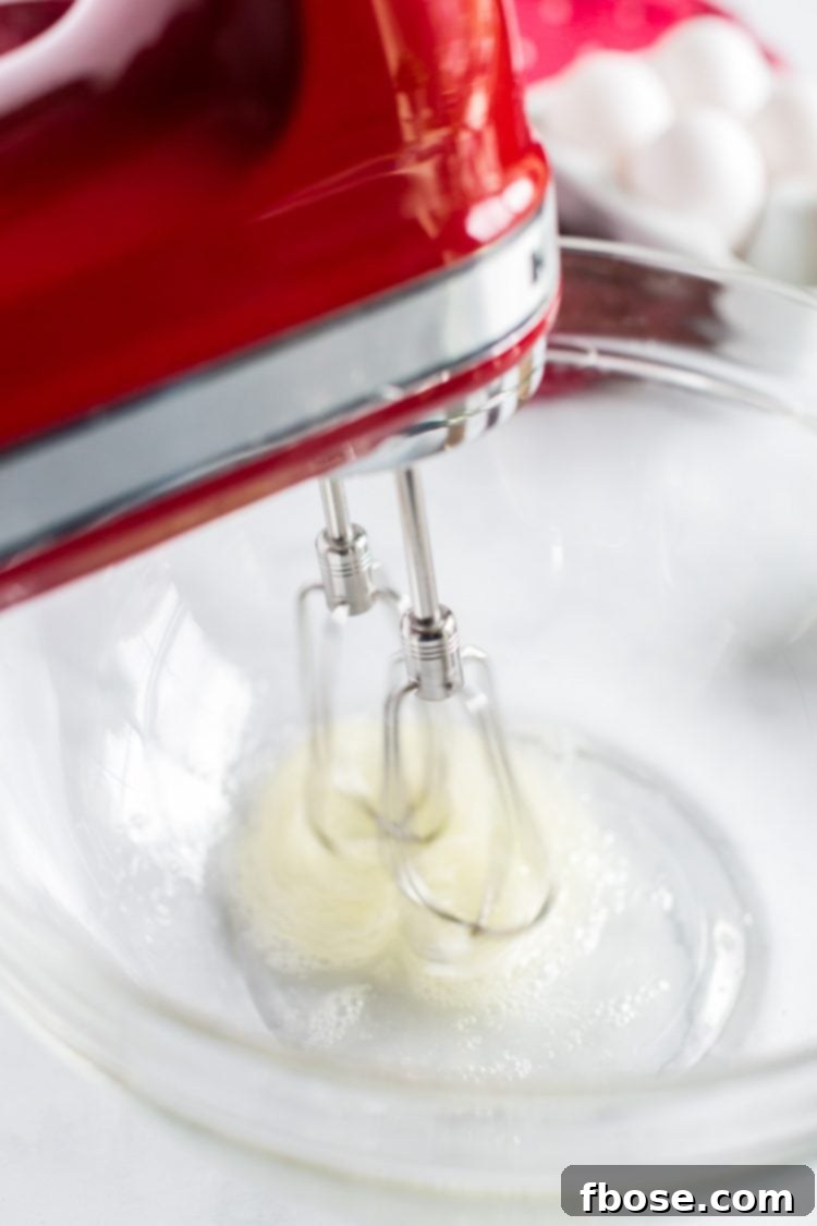 Egg whites being beaten with a hand mixer in a glass bowl until foamy.