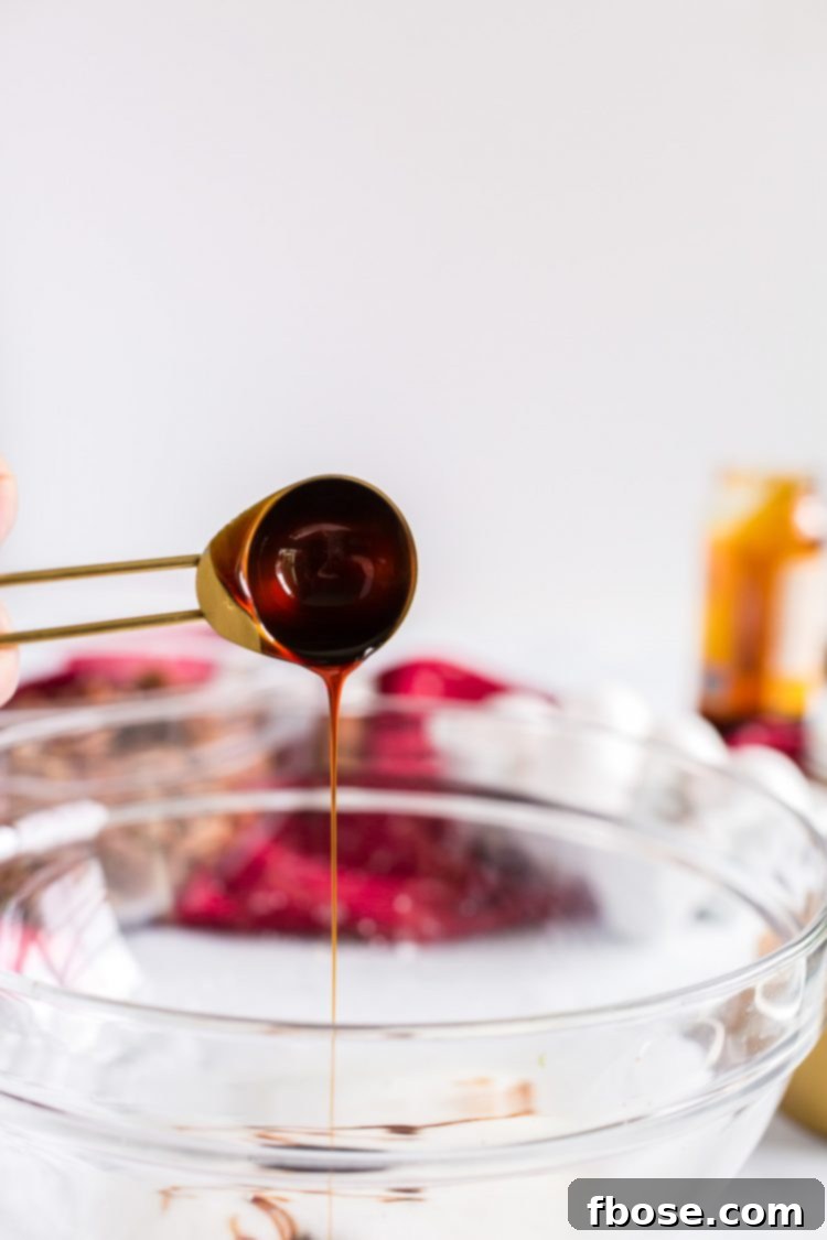 Molasses being added to a glass mixing bowl with foamy egg whites.