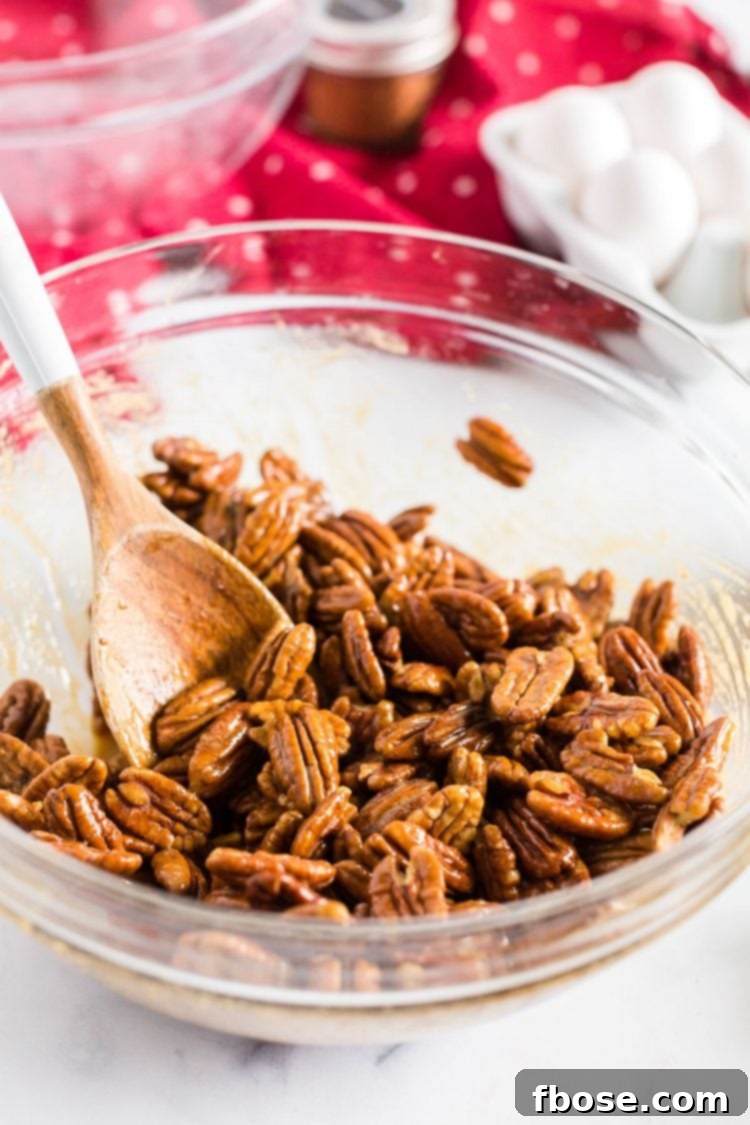 Pecans in a mixing bowl being tossed with a wooden spoon to coat them evenly.