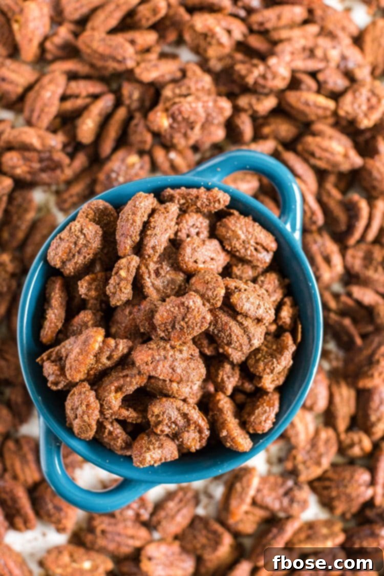 Overhead photo of a blue bowl filled with gingerbread candied pecans, with more scattered around.