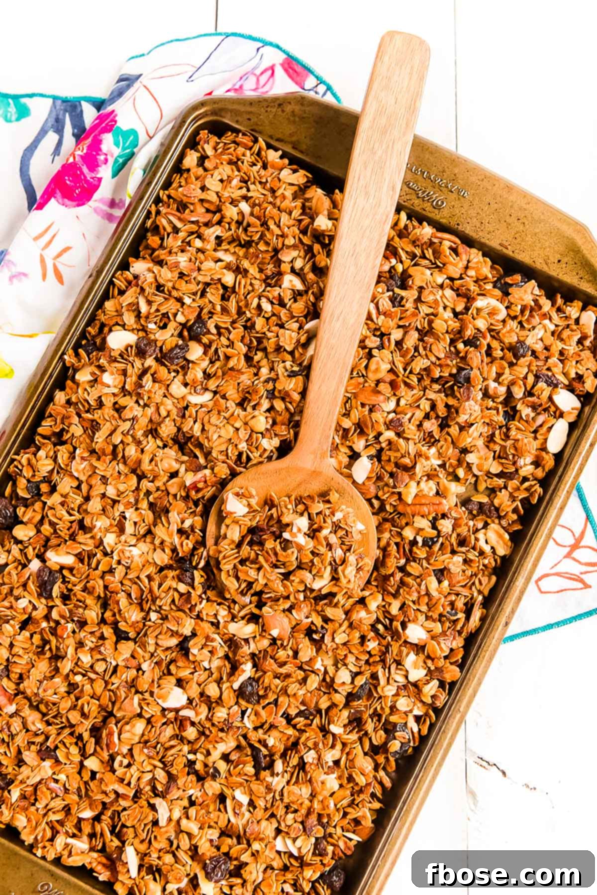 Homemade granola on a sheet pan with a wooden spoon scooping it.