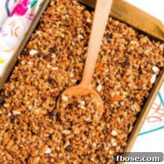 Homemade granola on a sheet pan with a wooden spoon scooping it.