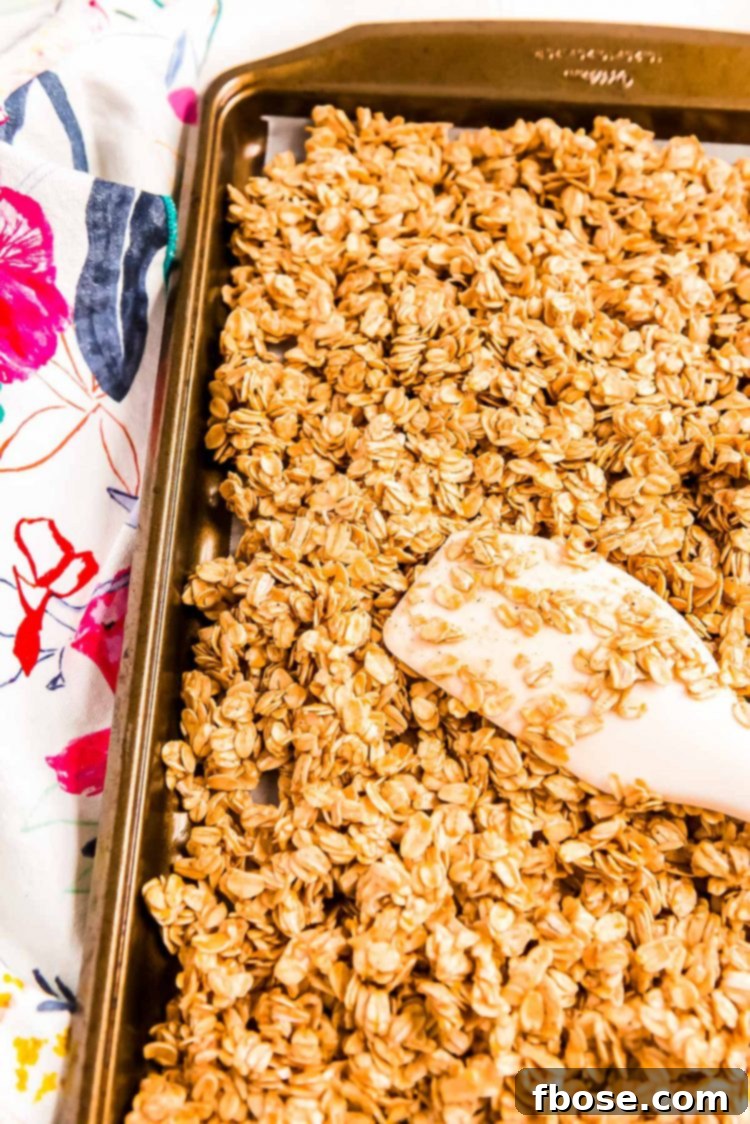 Oats being spread out on a large baking sheet with a rubber spatula to make granola.