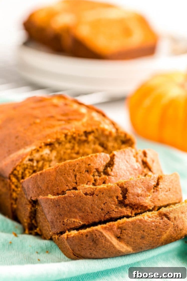 A beautifully baked loaf of pumpkin cream cheese bread, partially sliced to reveal the vibrant orange pumpkin and creamy white swirl, resting on a rustic blue napkin.