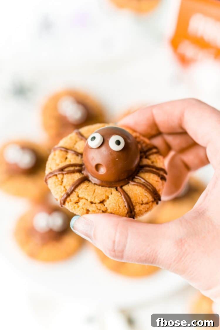 Woman's hand holding a peanut butter cookie decorated like a spider for Halloween.