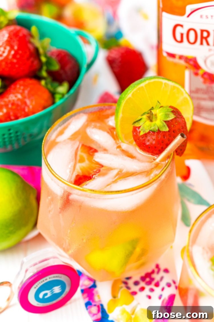 Close up photo of a pink gin spritz in a gold rimmed glass garnished with a lime and strawberry.