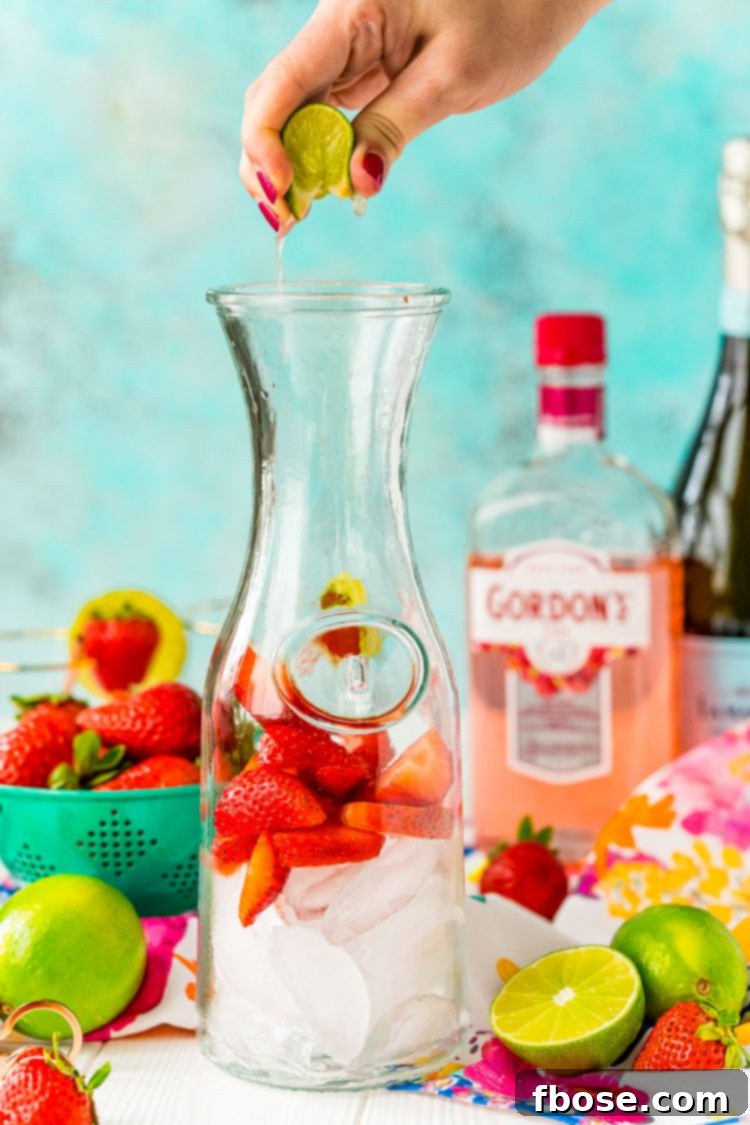 Woman's hand squeezing lime juice into a carafe with strawberries and ice.