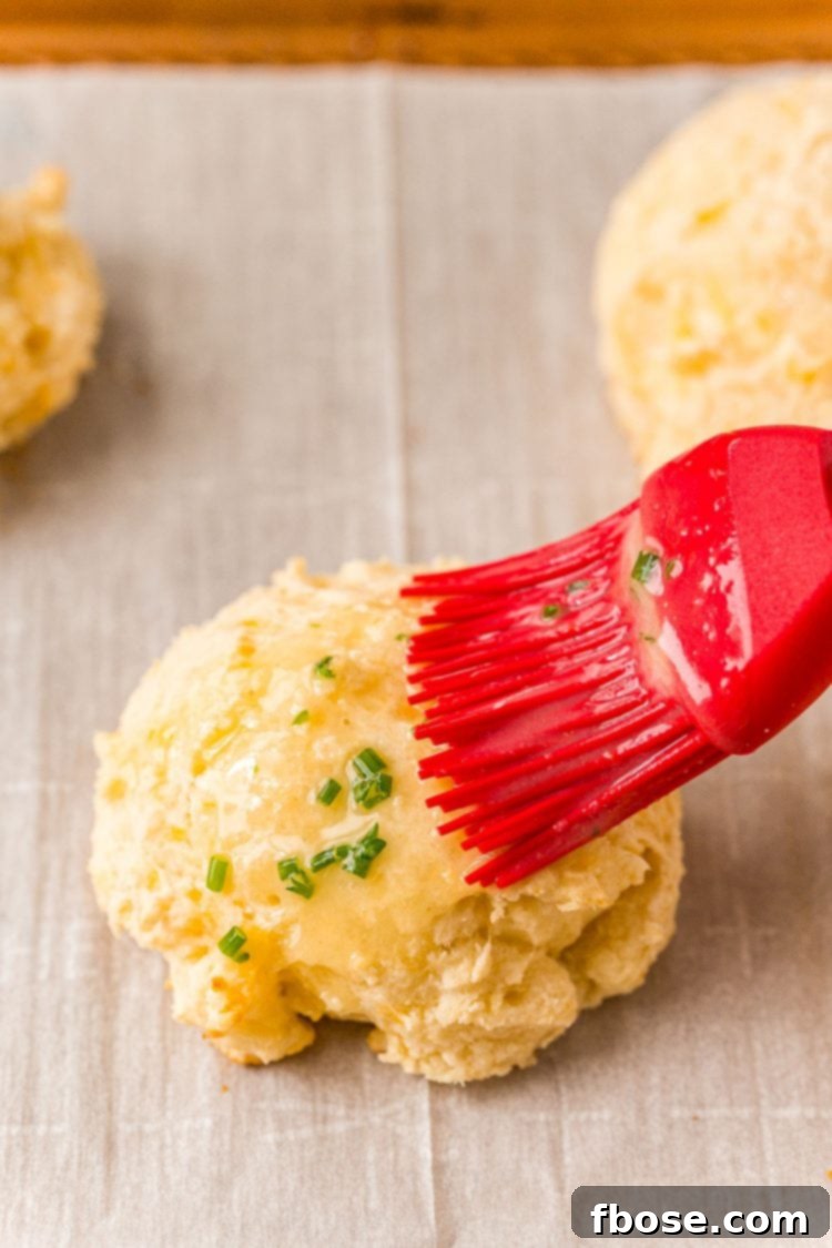A pastry brush brushing butter on a biscuit.