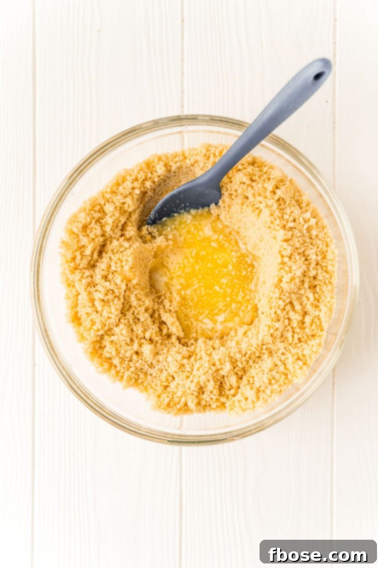 Cookie crumbs in a bowl with melted butter and a mixing spoon.