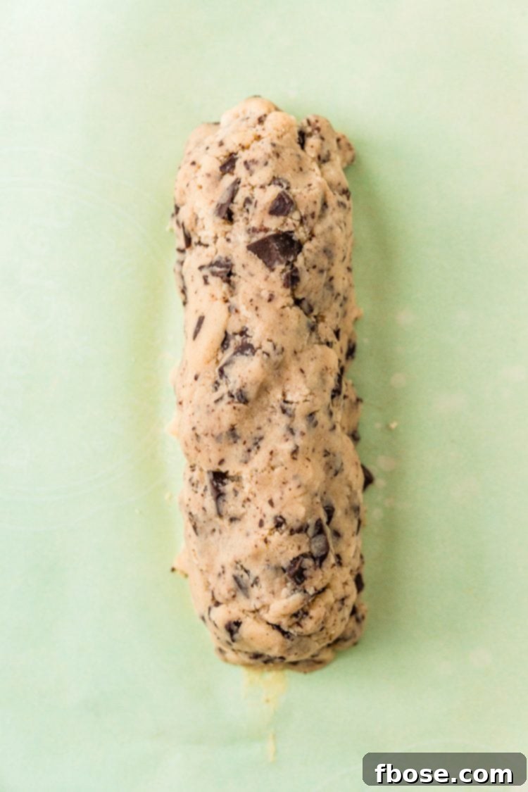 Chocolate chunk cookie dough formed into a log on parchment paper.