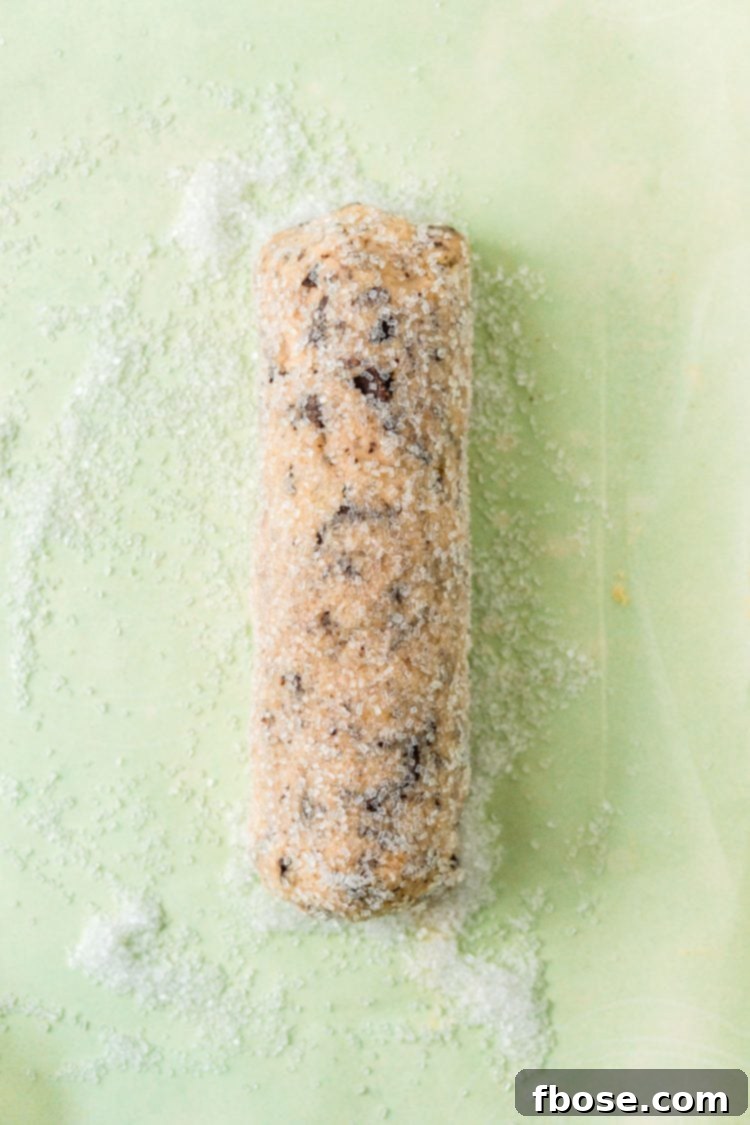 Log of cookie dough rolled in coarse sugar on parchment paper.