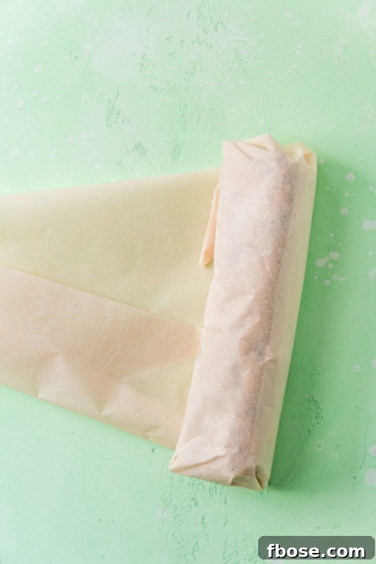 Cookie dough being rolled up in parchment paper.
