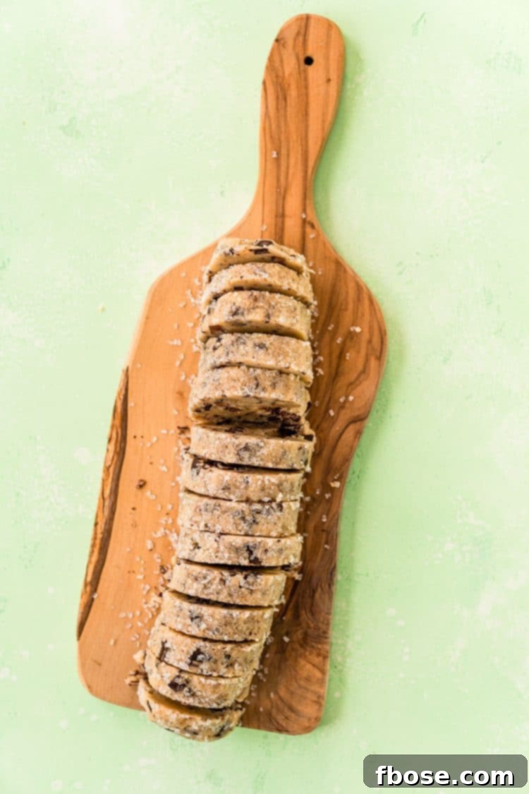 Log of cookie dough that has been sliced for baking on a cutting board.
