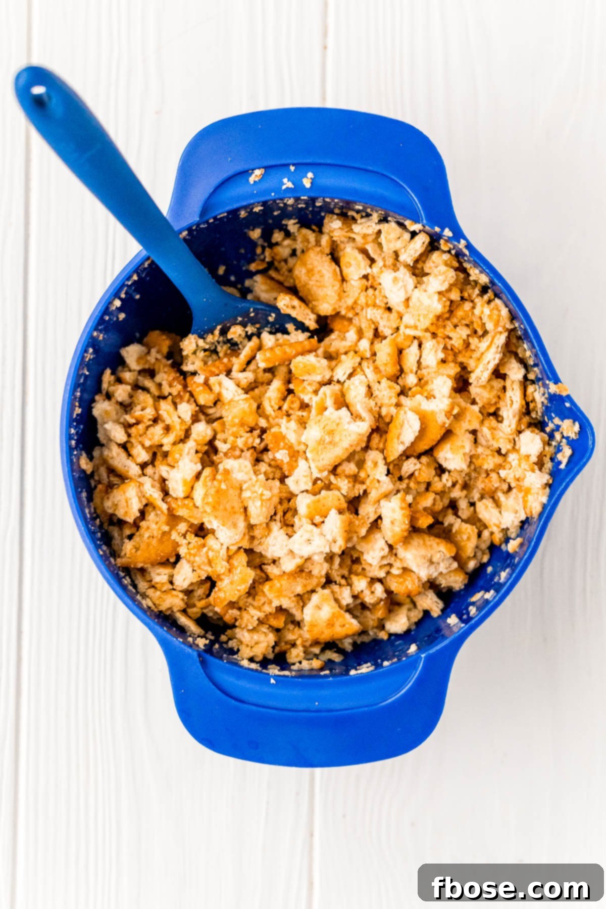 Crushed crackers and butter being mixed in a blue bowl.
