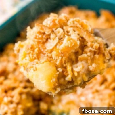 A wooden serving spoon lifting a scoop of pineapple casserole out of a serving dish.