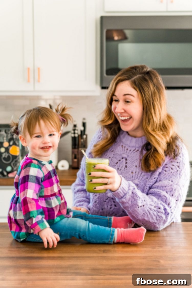 Toddler girl and her mother sharing a smoothie in the kitchen.