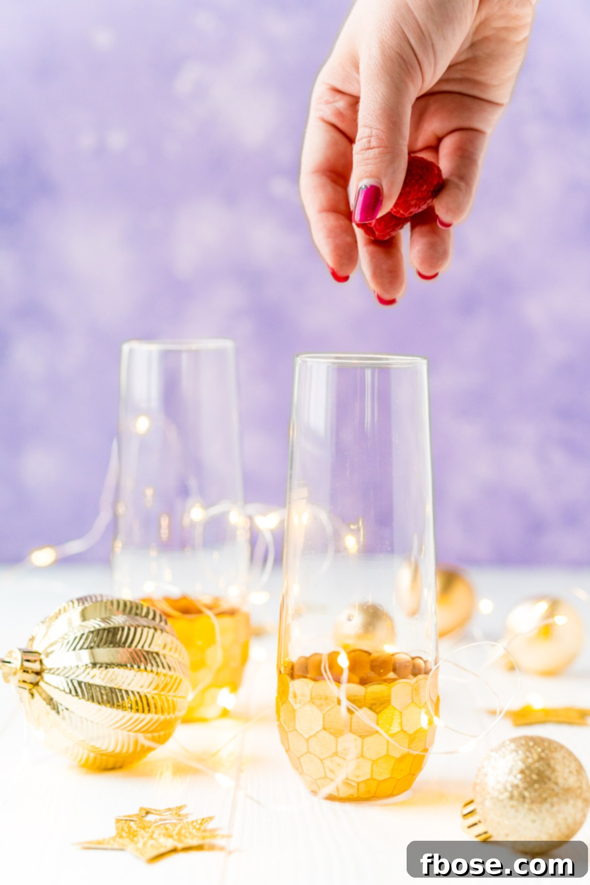 Golden Bloom Fizz 3 Woman's hand dropping fresh raspberries into a champagne flute to make a cocktail.