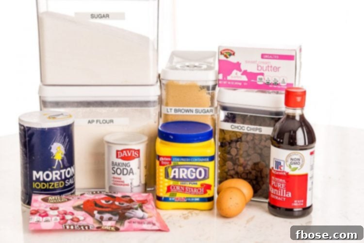 A vibrant flat lay of essential ingredients for chocolate chip cookie bars, including flour, sugar, butter, eggs, chocolate chips, and colorful M&M's, arranged on a rustic wooden table.