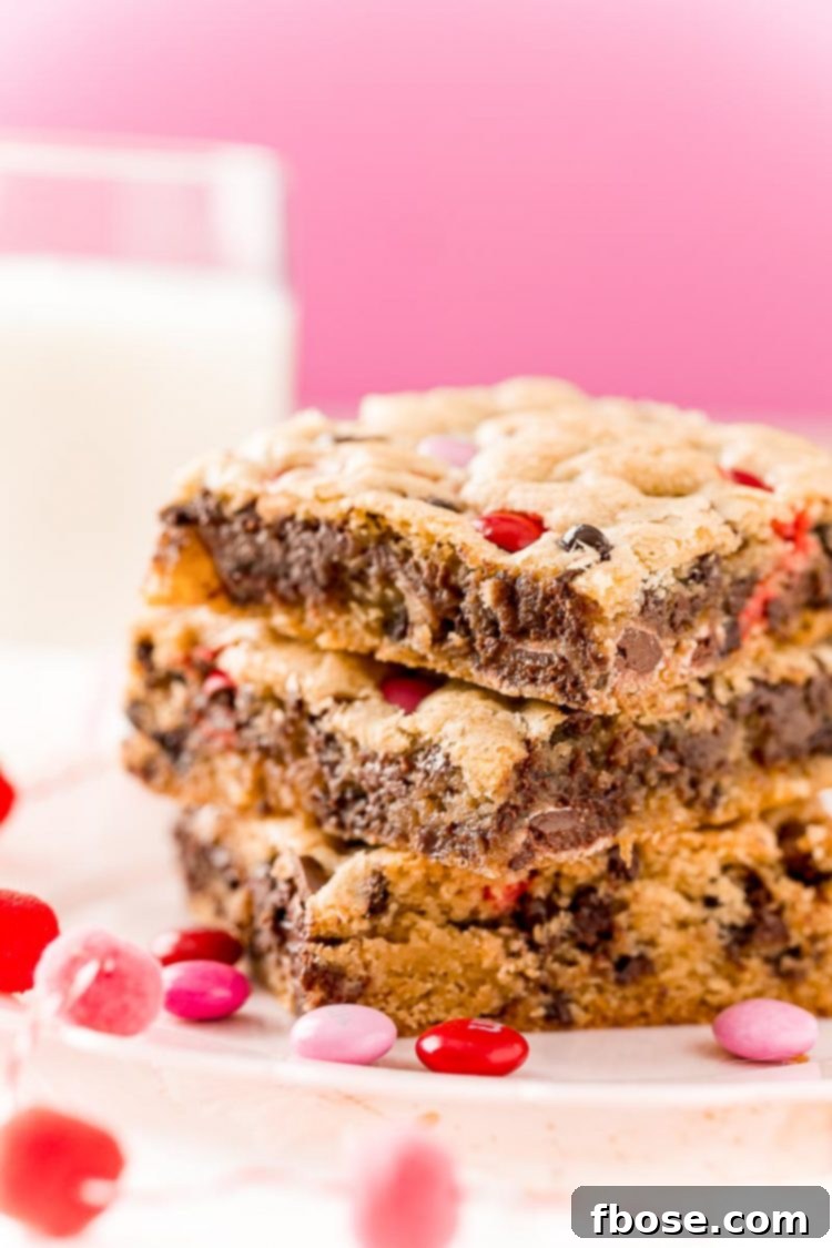 Three perfectly baked chocolate chip cookie bars, studded with vibrant M&M's, stacked for display, highlighting their appealing texture and rich color.
