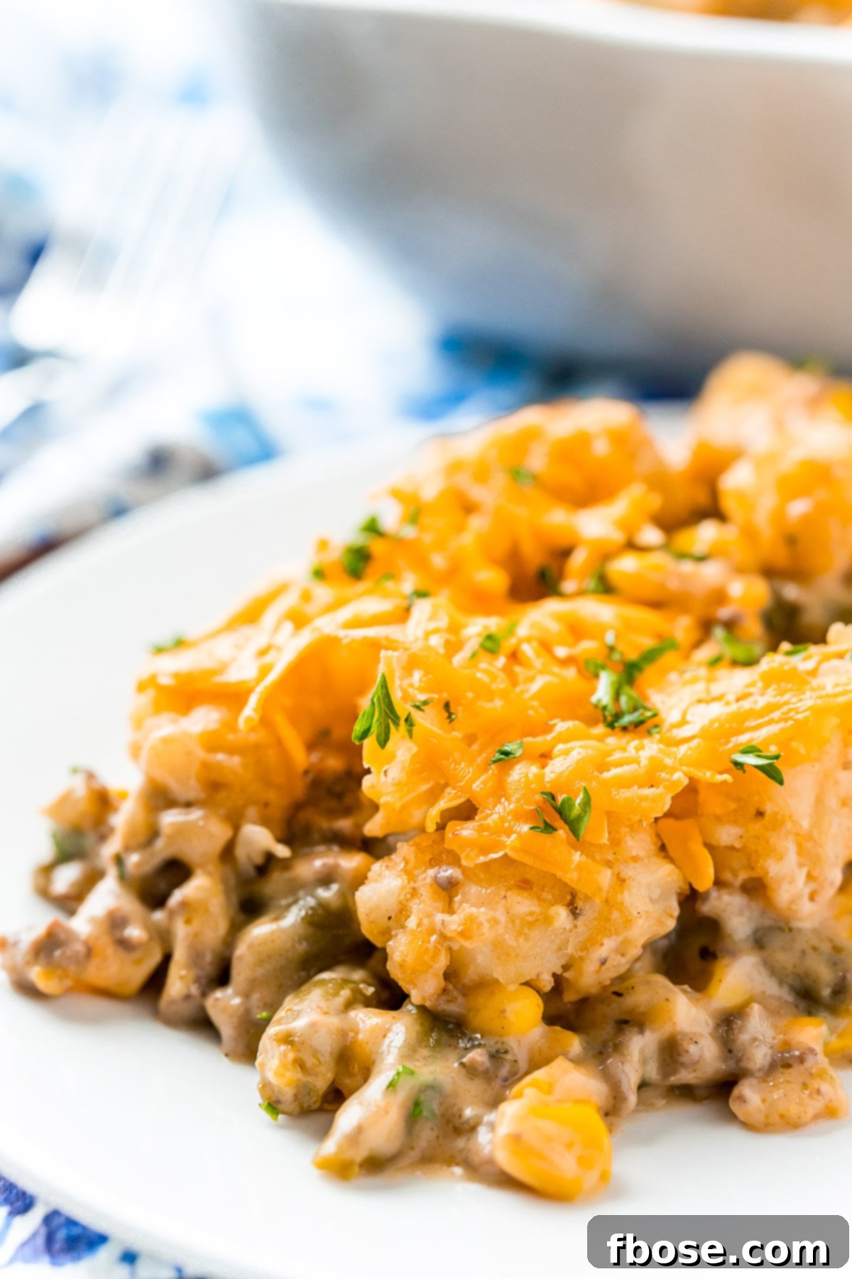 A scoop of tater tot casserole on a white plate on a blue napkin.