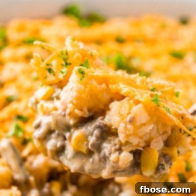 Close up photo of a serving spoon scooping tater tot hotdish out of a casserole dish.