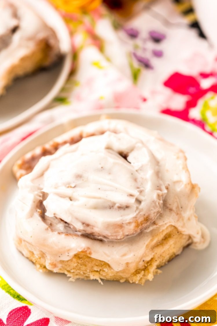 A single, perfectly baked cinnamon roll with generous icing, presented on a minimalist white plate.