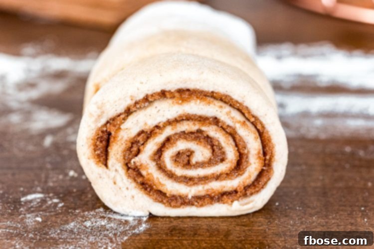 Unbaked cinnamon roll dough, perfectly rolled and ready to be sliced, showcasing the distinct layers of cinnamon sugar filling.
