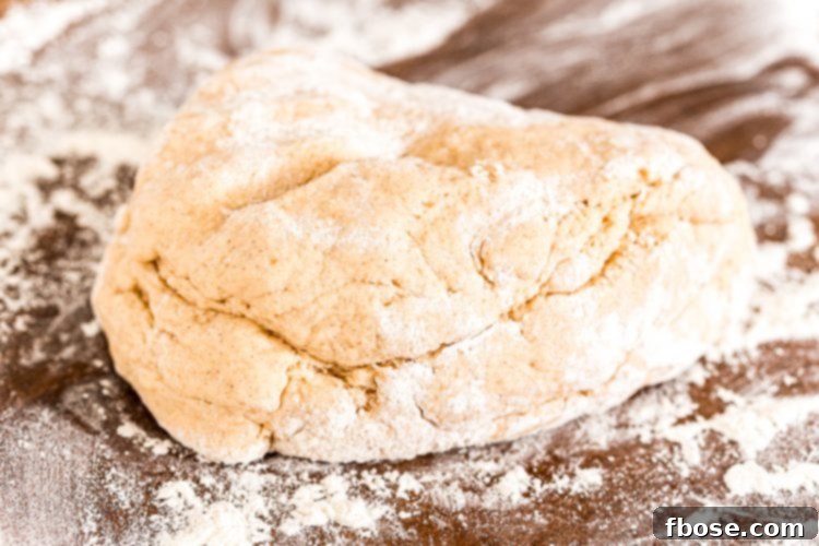 A ball of cinnamon roll dough resting on a floured surface, ready to be rolled out.