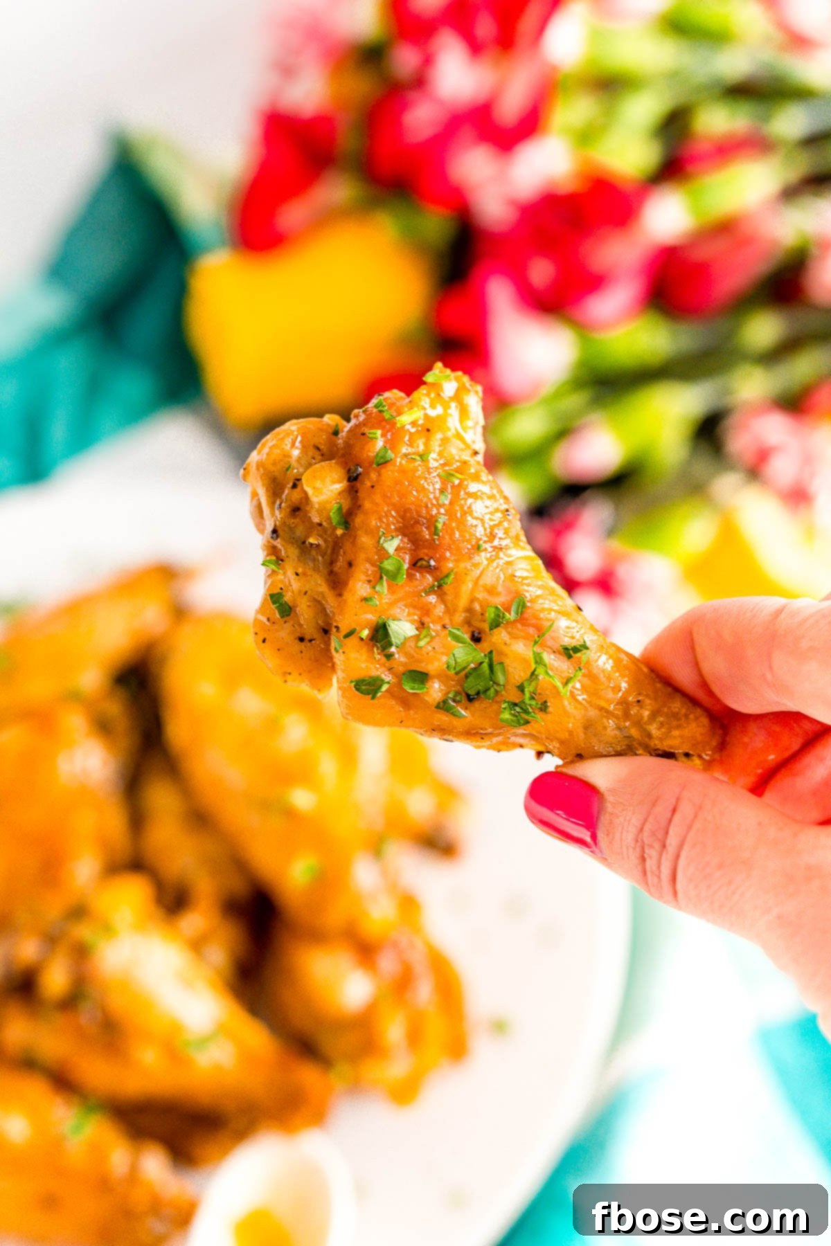 Crispy Oven Baked Wings 4 Woman's hand gracefully holding a perfectly baked, golden-brown chicken wing, showcasing its crisp texture.