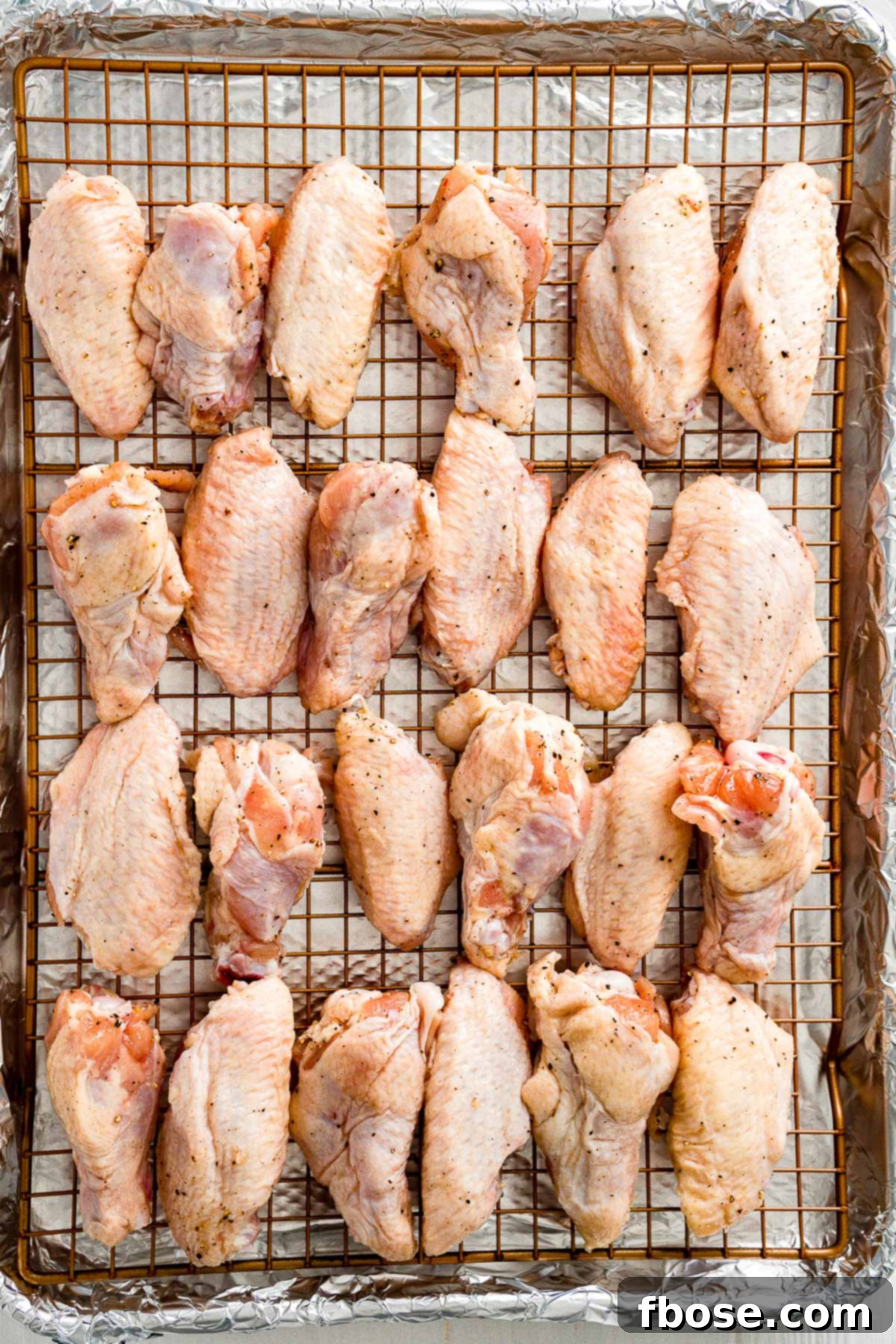 Crispy Oven Baked Wings 5 Uncooked chicken wings meticulously arranged in a single layer on a wire rack over a baking sheet, ready for the oven.