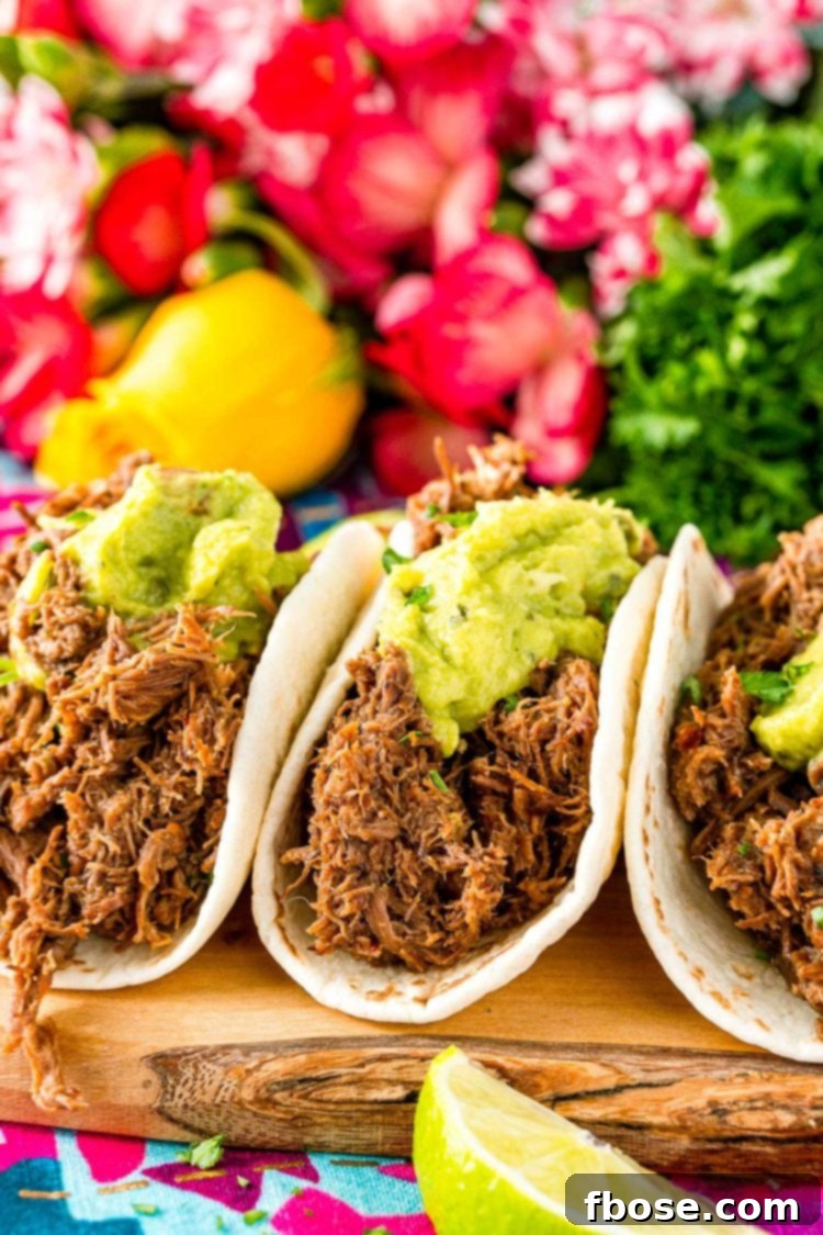 Close up photo of tacos made with barbacoa beef and topped with guacamole. Pink flowers in the background.
