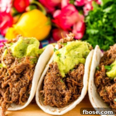 Close up photo of three barbacoa tacos on a cutting board with pink flowers in the background.