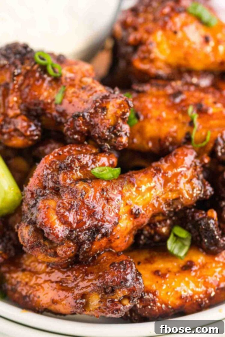 Close up photo of chicken wings coated in a sticky sauce and topped with scallions.