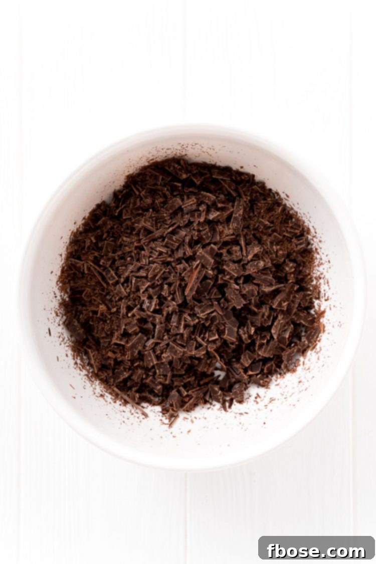 Finely chopped dark chocolate pieces resting in a white ceramic bowl, ready for the next step.