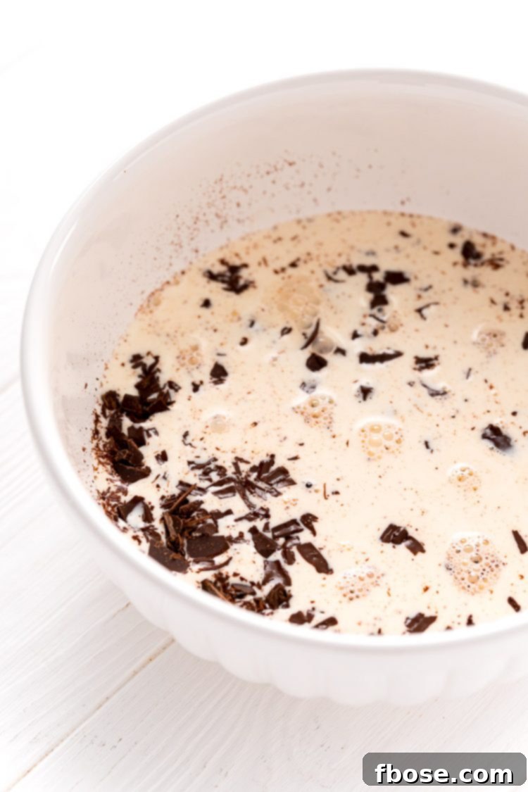 White bowl with finely chopped chocolate and hot heavy cream, resting before being whisked.