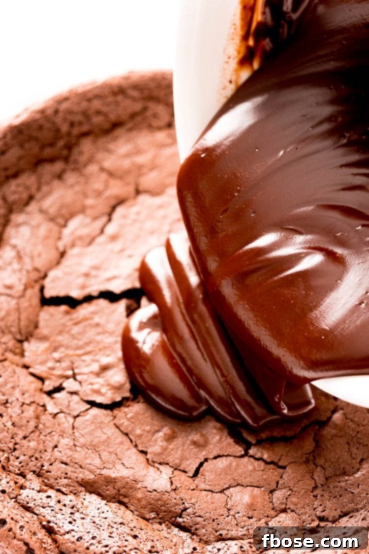 A rich stream of chocolate ganache being poured gracefully over the top of a decadent chocolate layer cake.