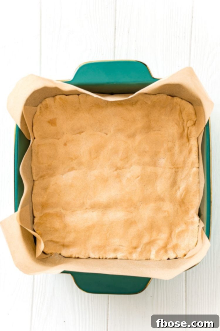 Overhead view of a square baking dish neatly filled with a pressed layer of peanut butter cookie dough, ready for the next step.