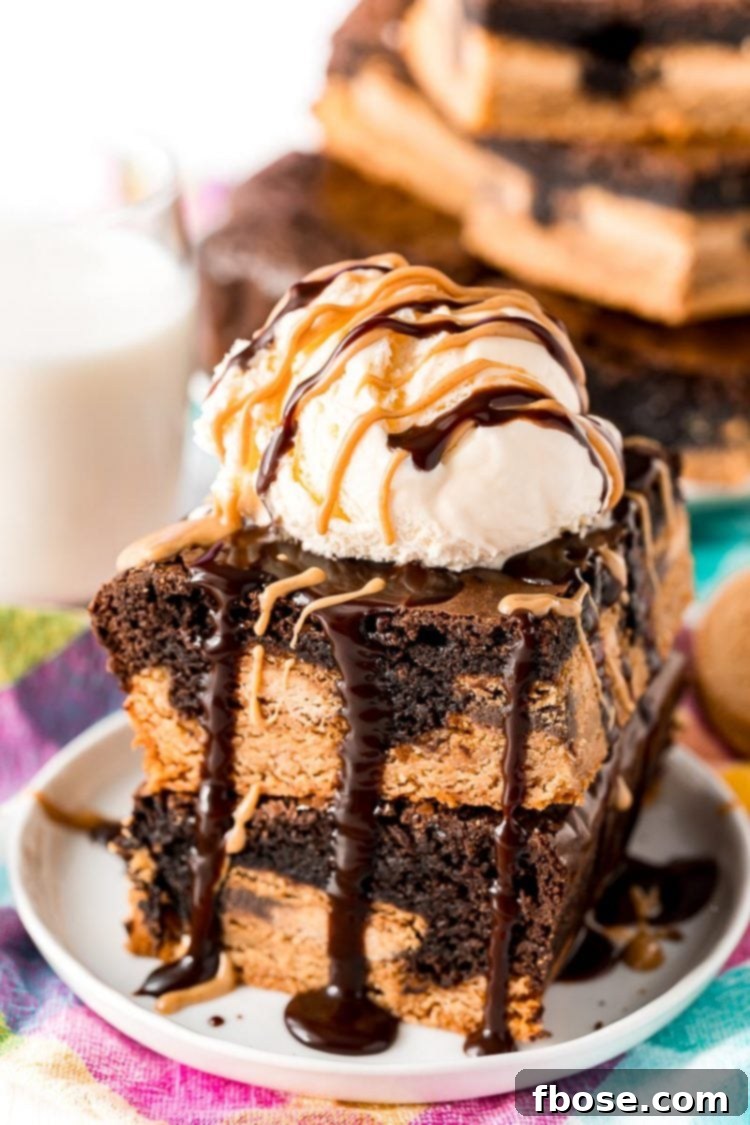 Close-up of decadent Peanut Butter Oreo Brownies stacked high, generously topped with creamy ice cream, peanut butter sauce, and hot fudge.