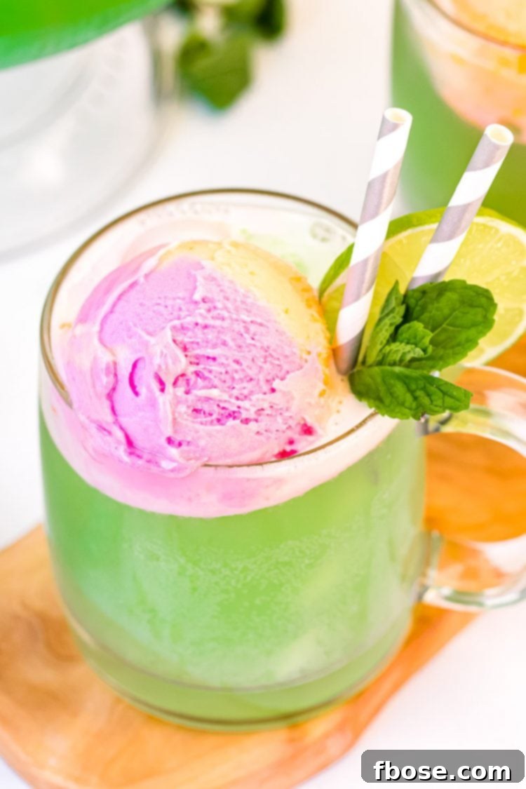 Whimsical Rainbow Sherbet Punch 5 Close up photo of a mug filling with green punch topped with rainbow sherbet and garnished with lime slice and mint, ready to be served.