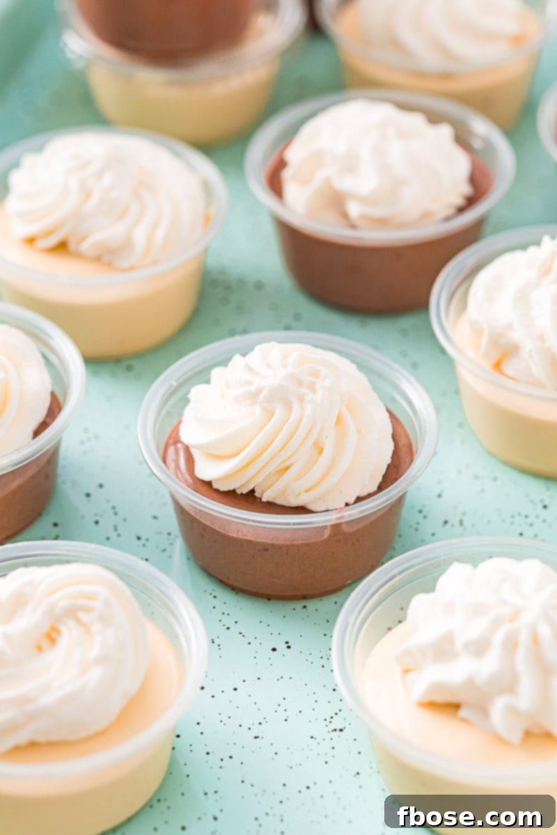 Close-up overhead photo of beautifully garnished pudding shots topped with whipped cream, arranged on a light blue cookie sheet.