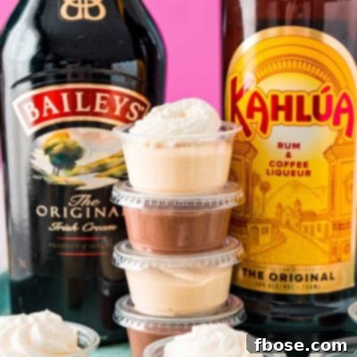 Stack of creamy pudding shots between a bottle of Baileys and a bottle of Kahlua.