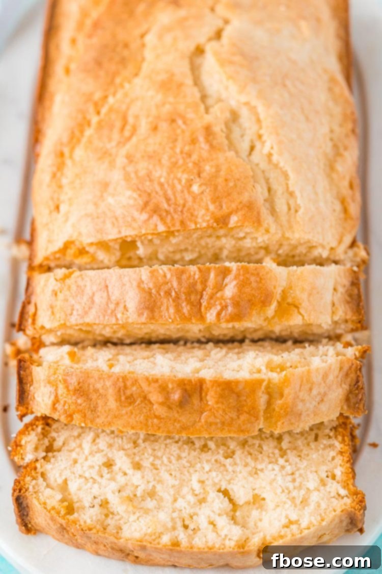A perfectly baked loaf of Ice Cream Bread rests on a pristine white cutting board, partially sliced to reveal its tender interior.