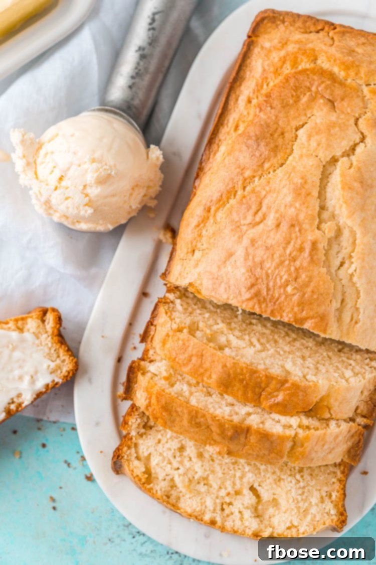An overhead view of a perfectly sliced loaf of ice cream bread sits beside an ice cream scoop filled with vanilla ice cream, ready to be enjoyed.