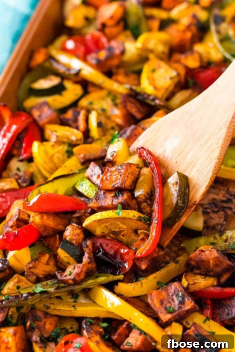 A wooden spatula scooping perfectly roasted vegetables, including sweet potatoes and bell peppers, off a sheet pan, showcasing their golden-brown caramelization.