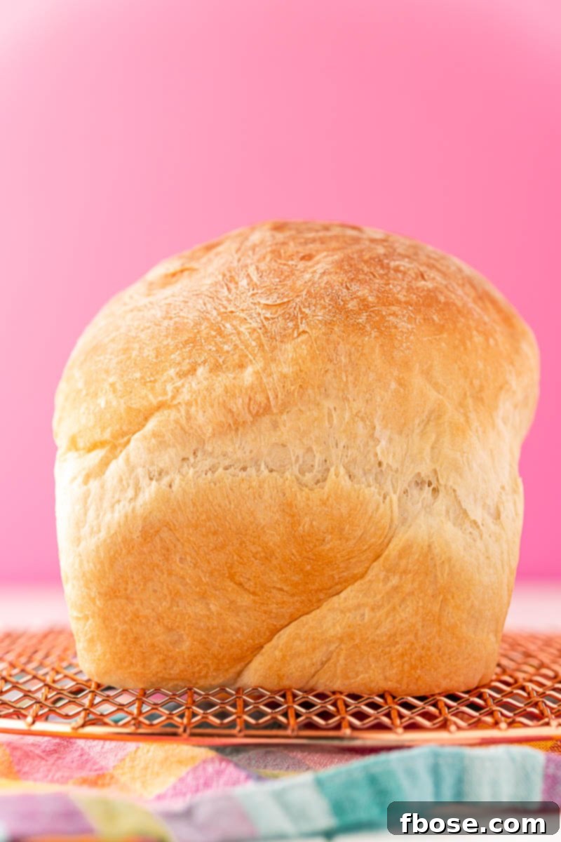 A freshly baked loaf of fluffy white bread resting on a cooling rack over a vibrant, colorful napkin, ready to be sliced and enjoyed.