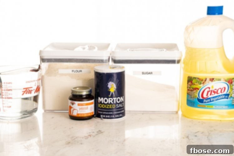 Various baking ingredients including flour, sugar, salt, and yeast laid out on a clean marble table, ready for bread making.