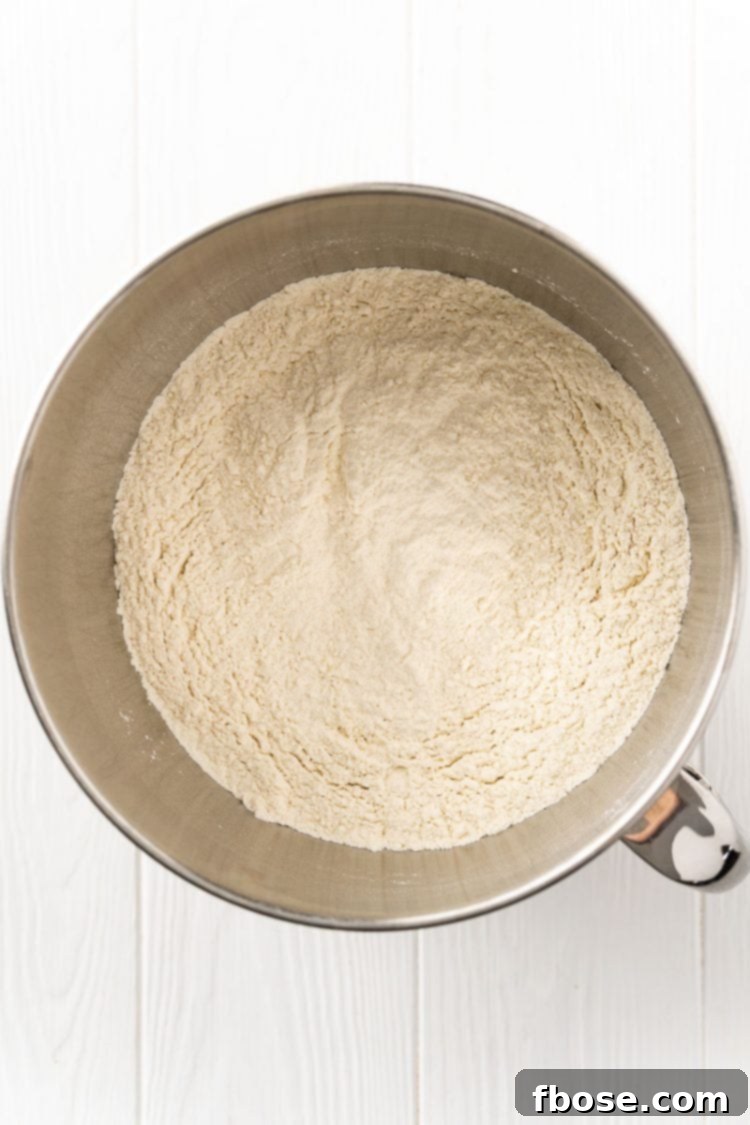 Dry ingredients for bread making, including flour, sugar, and yeast, neatly combined in a stand mixer bowl, ready for liquid.