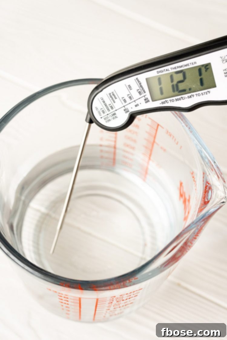 A digital thermometer accurately measuring the temperature of water in a clear measuring cup, ensuring optimal warmth for yeast activation.